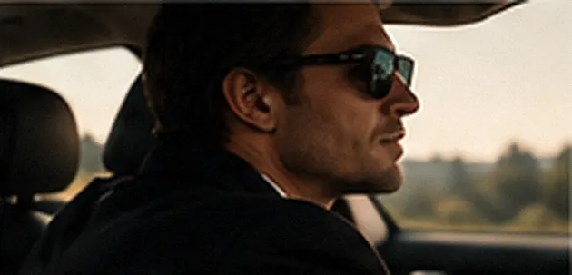 A man in sunglasses at the wheel of a car in warm evening light